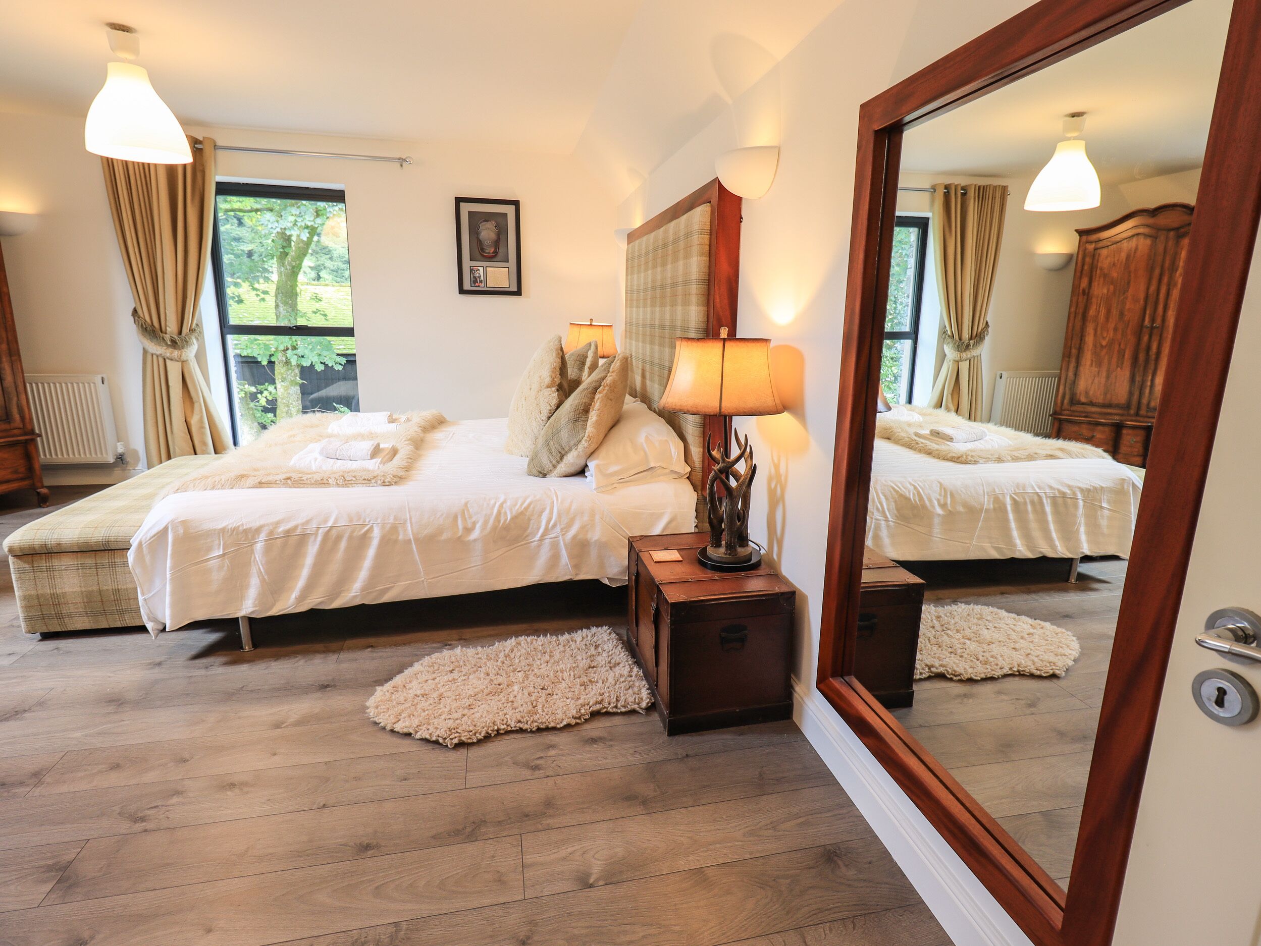 A bedroom with a large bed, a nightstand, a mirror, and a window with curtains.