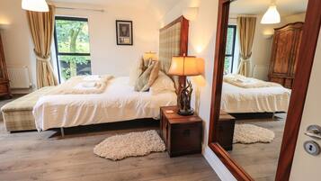 A bedroom with a large bed, a nightstand, a mirror, and a window with curtains.