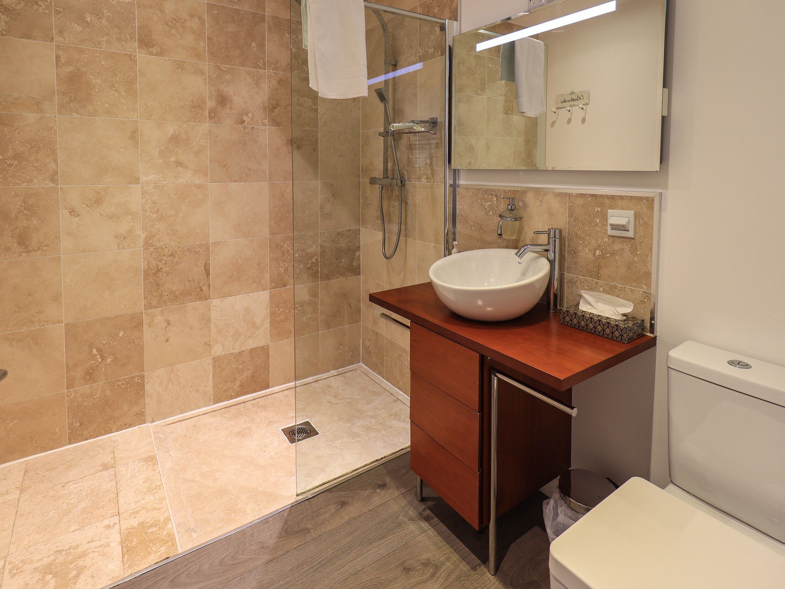 A modern bathroom with a large sink, a shower, and a toilet.