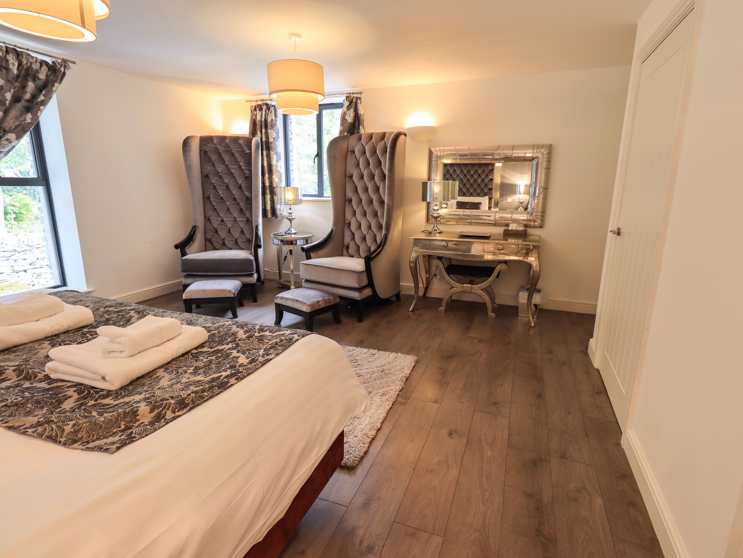 Una habitación de hotel con una cama grande, dos sillones, un tocador con espejo y un escritorio.