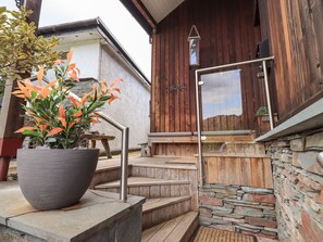 Une façade en bois, un mur en pierre et un escalier en métal menant à une terrasse en bois.