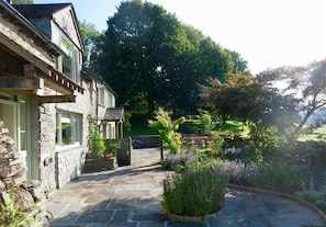 A stone building with a stone pathway leading to a garden area with various plants and a wooden fence.