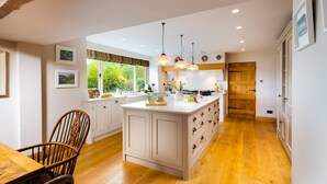 Une cuisine moderne avec des meubles en bois, un îlot central, des luminaires suspendus et une vue sur la verdure à l’extérieur.