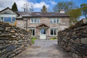 Une maison en pierre avec une entrée centrale, des murs en pierre et un chemin dallé menant à la porte.