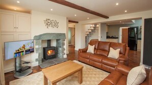 A living room with a stone fireplace, leather sofa, and a television. - Dancing Beck Cottage (Keswick)