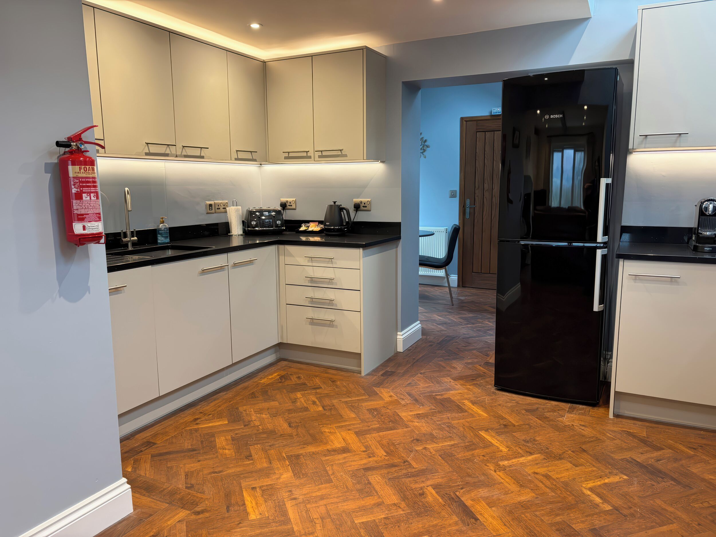 A modern kitchen with white cabinets, a black refrigerator, and a herringbone wood floor.
