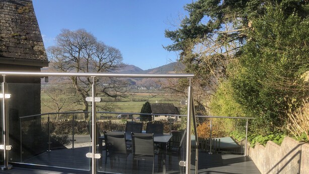 A glass-enclosed outdoor seating area with a view of a rural landscape. - Dancing Beck Cottage (Keswick)