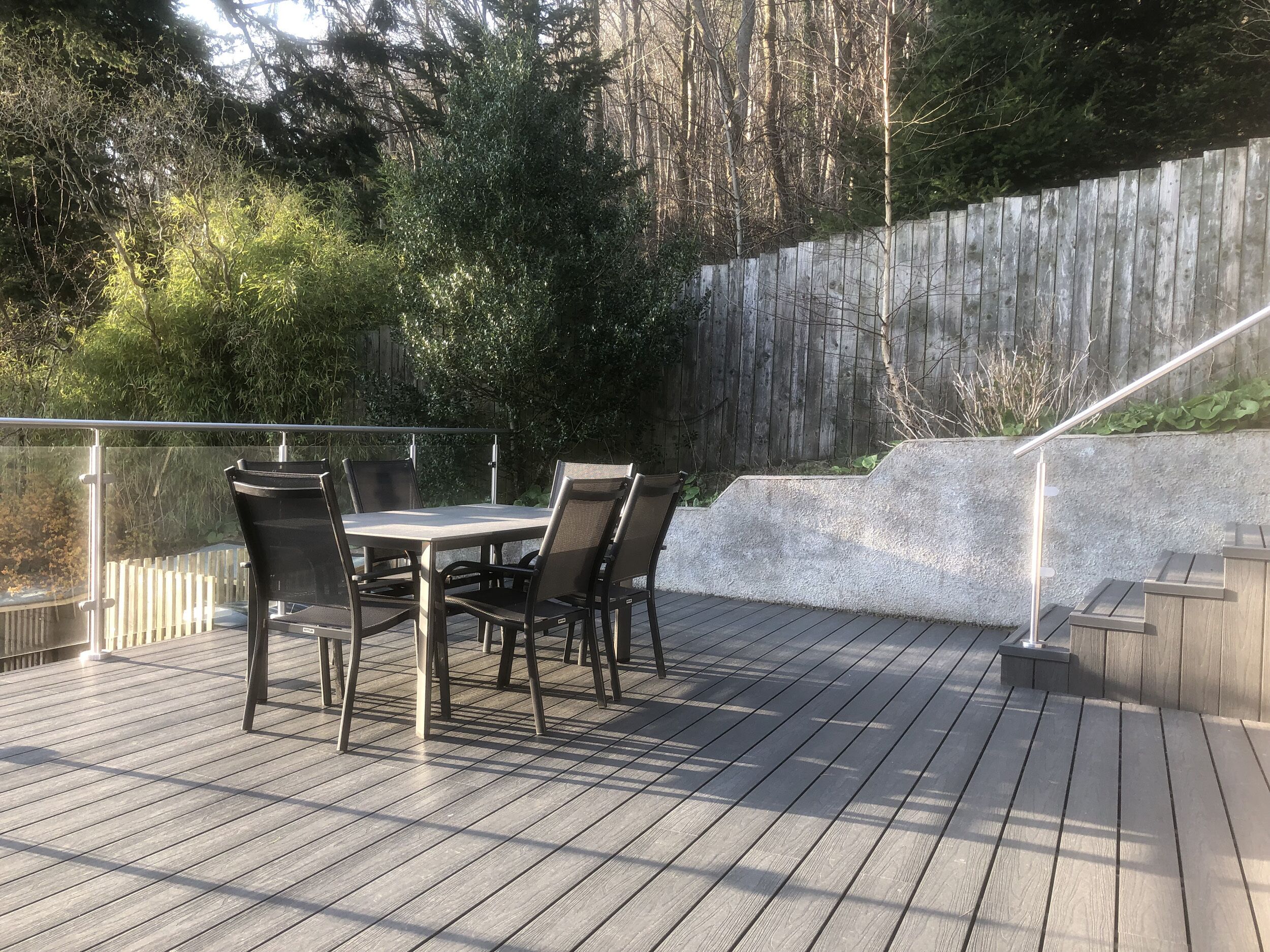 Una terraza con una mesa y sillas, rodeada por una valla de madera y árboles.