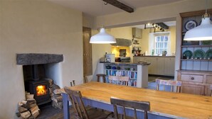 A rustic kitchen with a wood-burning stove, a long wooden table, and chairs. - Thomas Grove House (Penrith)