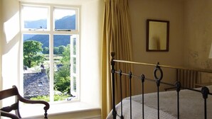 A bedroom with a large window, a bed, a chair, and a mirror on the wall. - Thomas Grove House (Penrith)
