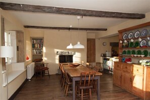 A rustic kitchen with a wooden table, chairs, a bookshelf, and a cabinet with dishes. - Thomas Grove House (Penrith)