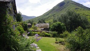 A stone house with a stone pathway leading to a grassy area, surrounded by lush greenery and a mountain in the background. - Thomas Grove House (Penrith)