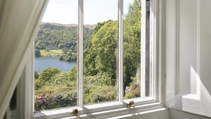 A room with a large window offering a view of a lake surrounded by lush greenery and hills. - Wetherlam (Ambleside)