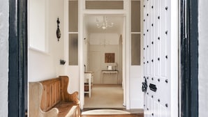 A hallway with a wooden bench, a white door with black studs, and a chandelier in the background. - Wetherlam (Ambleside)