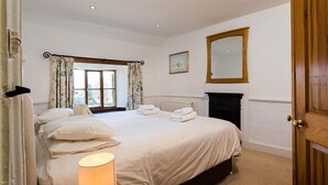 Un dormitorio con una cama grande, una chimenea, una ventana con cortinas y un espejo en la pared.