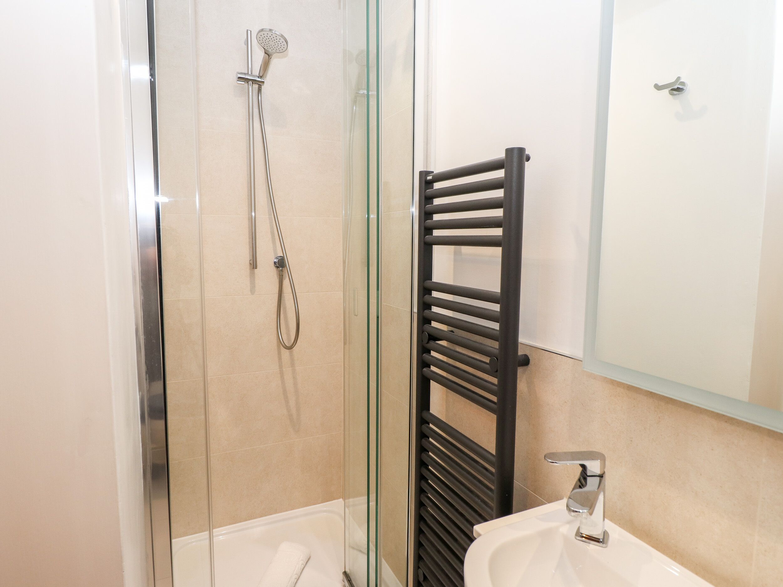 A modern bathroom with a glass-enclosed shower, a black towel rack, and a white sink.