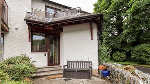 A house with a stone wall, a wooden bench, and a garden. - Chapelside Cottage (Ambleside)