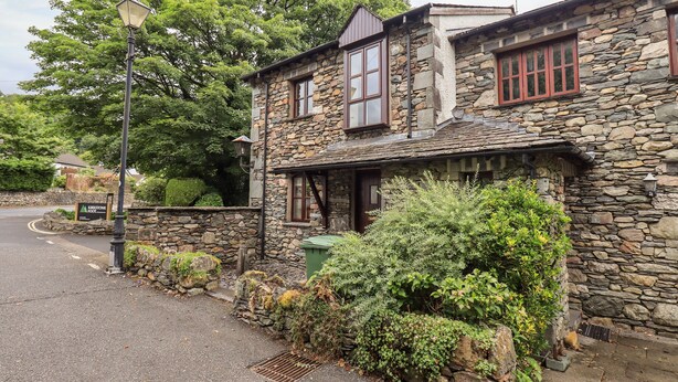 A stone building with a traditional design, featuring a stone facade, multiple windows, and a small porch area. - Chapelside Cottage (Ambleside)