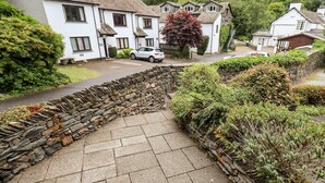 A stone wall with a paved area, surrounded by greenery and residential buildings. - Chapelside Cottage (Ambleside)