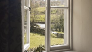 A view through a window of a rural landscape with a stone wall, grassy fields, and a river. - Yew Tree Farm (Coniston)