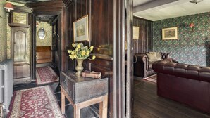 A traditional room with a wooden floor, a red sofa, a wooden cabinet, and a floral wallpaper. - Yew Tree Farm (Coniston)
