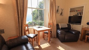 A living room with a sofa, a dining table with chairs, a TV, and a bookshelf. - Easedale (Ambleside)