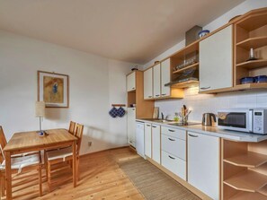 Una cocina pequeña con armarios blancos, una mesa de comedor de madera y un microondas.