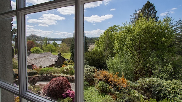 Une vue à travers une fenêtre sur un paysage rural, avec un lac, des arbres et un bâtiment en pierre.