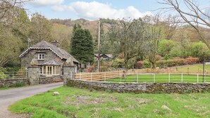 A stone cottage with a thatched roof, a stone wall, and a fenced paddock. - North Lodge (Ambleside)