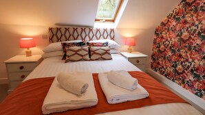 A neatly made bed with two folded towels, a window above the bed, and a floral-patterned wall. - North Lodge (Ambleside)