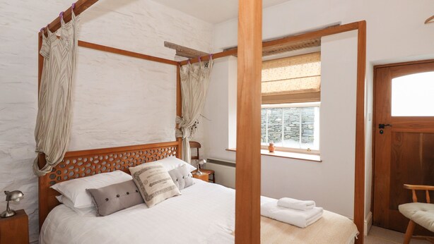 Ein Himmelbett mit Holz Kopfteil, weißer Bettwäsche und einem Fenster mit Blick auf eine Mauer.