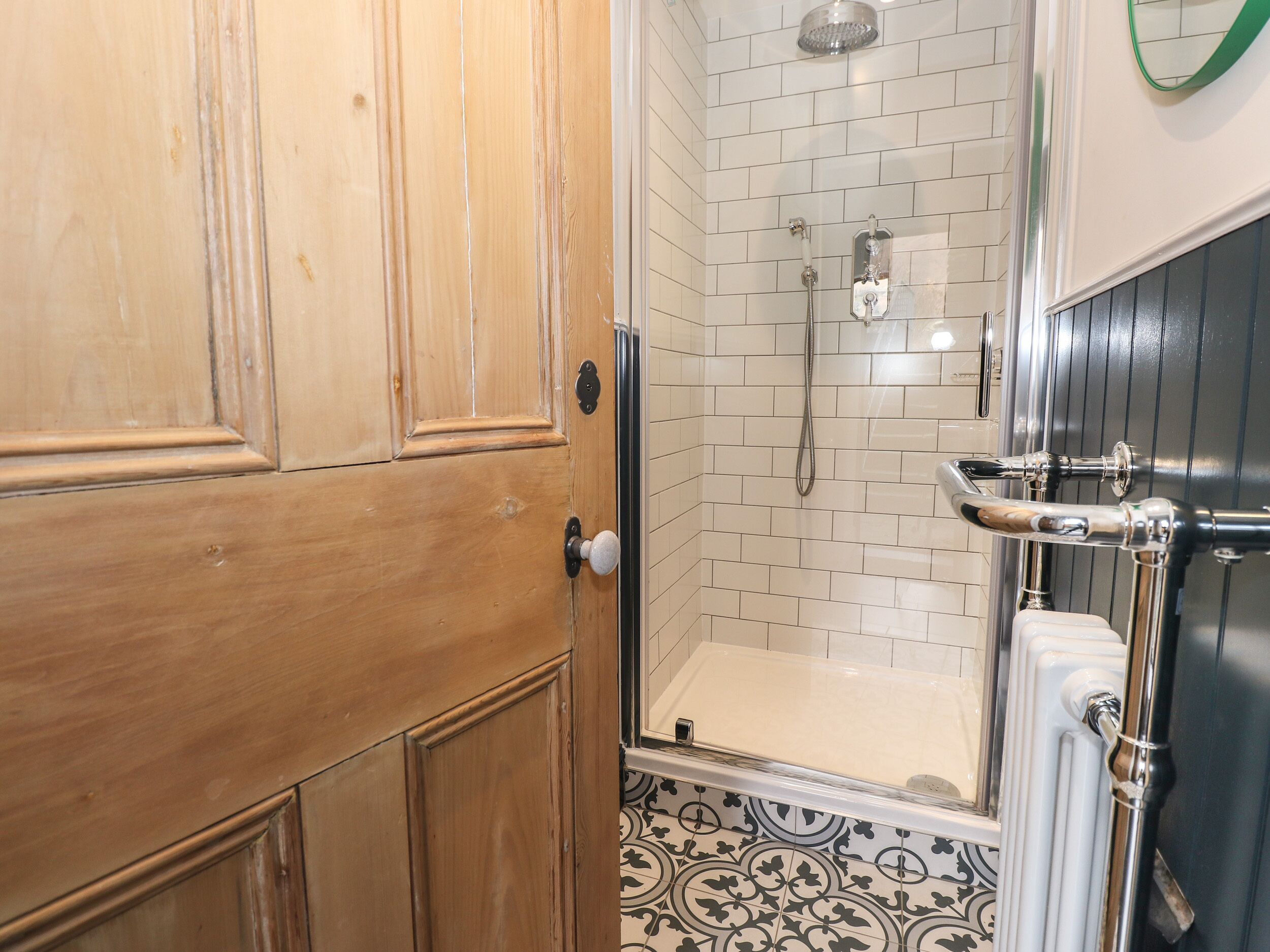 A bathroom with a wooden door, white tiled walls, a shower, and a radiator.