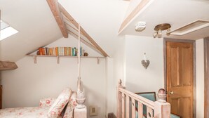 Ein gemütliches Schlafzimmer im Dachgeschoss mit einer Holztreppe, einem Bücherregal und einer blumigen Bettdecke.