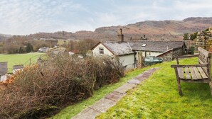 Ein ländliches Dorf mit Steinhäusern, einer grünen Wiese und Hügeln im Hintergrund.
