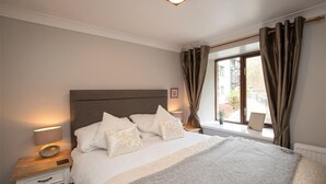 A neatly arranged bedroom with a bed, bedside lamps, and a window with curtains. - Over Ghyll (Ambleside)