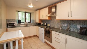 A modern kitchen with white cabinets, a microwave, a sink, and a window with a view of trees. - Over Ghyll (Ambleside)