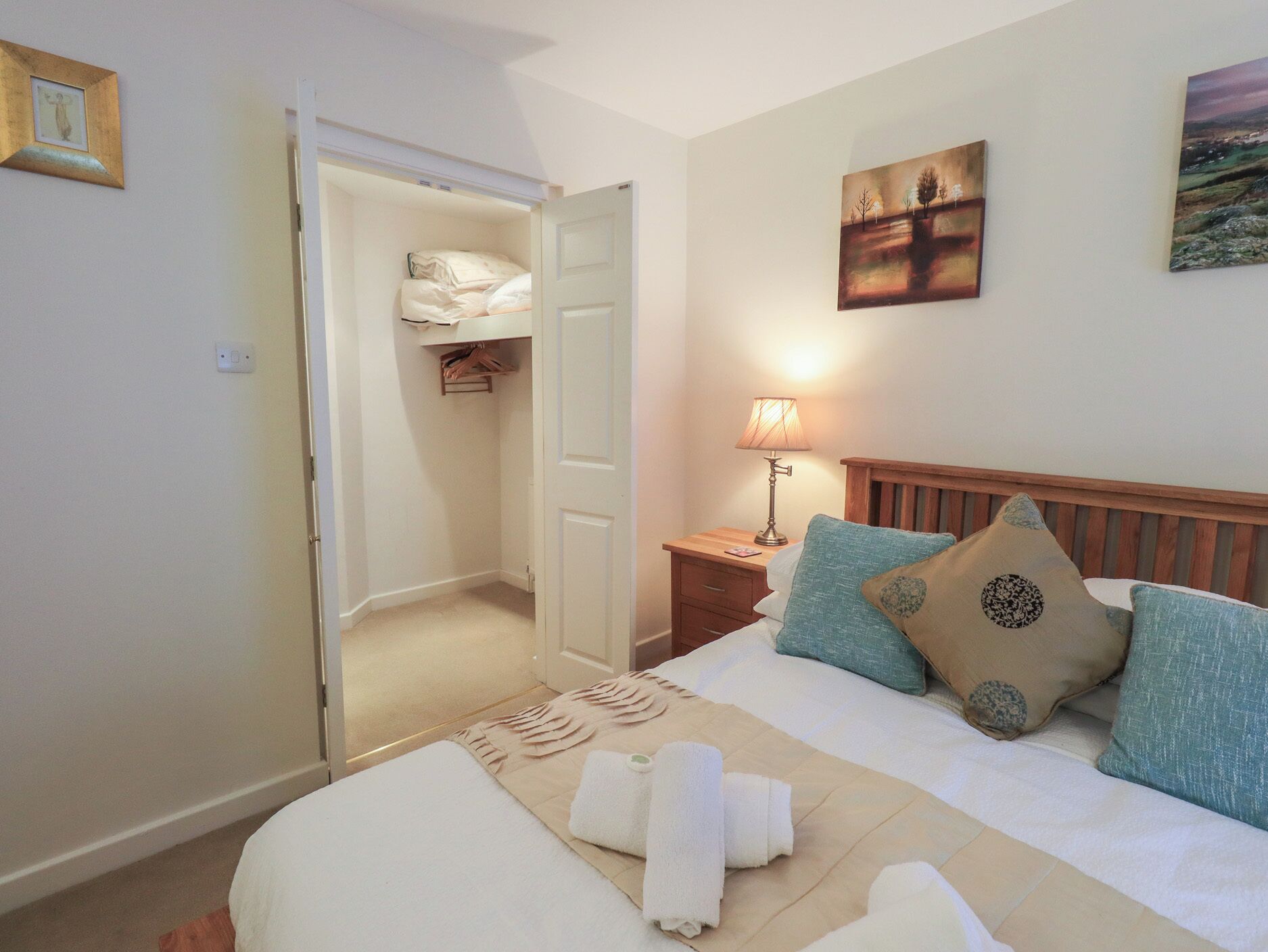 Una habitación de hotel con cama, mesita de noche con lámpara, armario y obras de arte en las paredes.