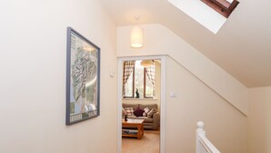 A hallway leading to a living room with a sofa, a table, and a window with curtains. There is a radiator on the wall and a framed picture above it. - Squirrel Bank (Ambleside)