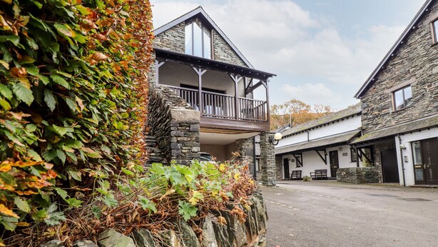 A stone building with a balcony, surrounded by ivy and a stone wall. - Squirrel Bank (Ambleside)