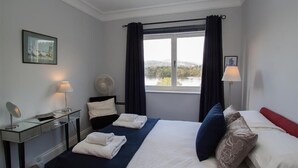 A hotel room with a bed, bedside table, lamp, and a view of the outdoors.