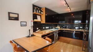A modern kitchen with a wooden dining table and chairs, black cabinets, and a built-in oven.