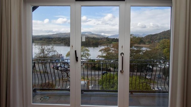 A balcony with a view of a lake and mountains, featuring a metal railing and a door with a handle.