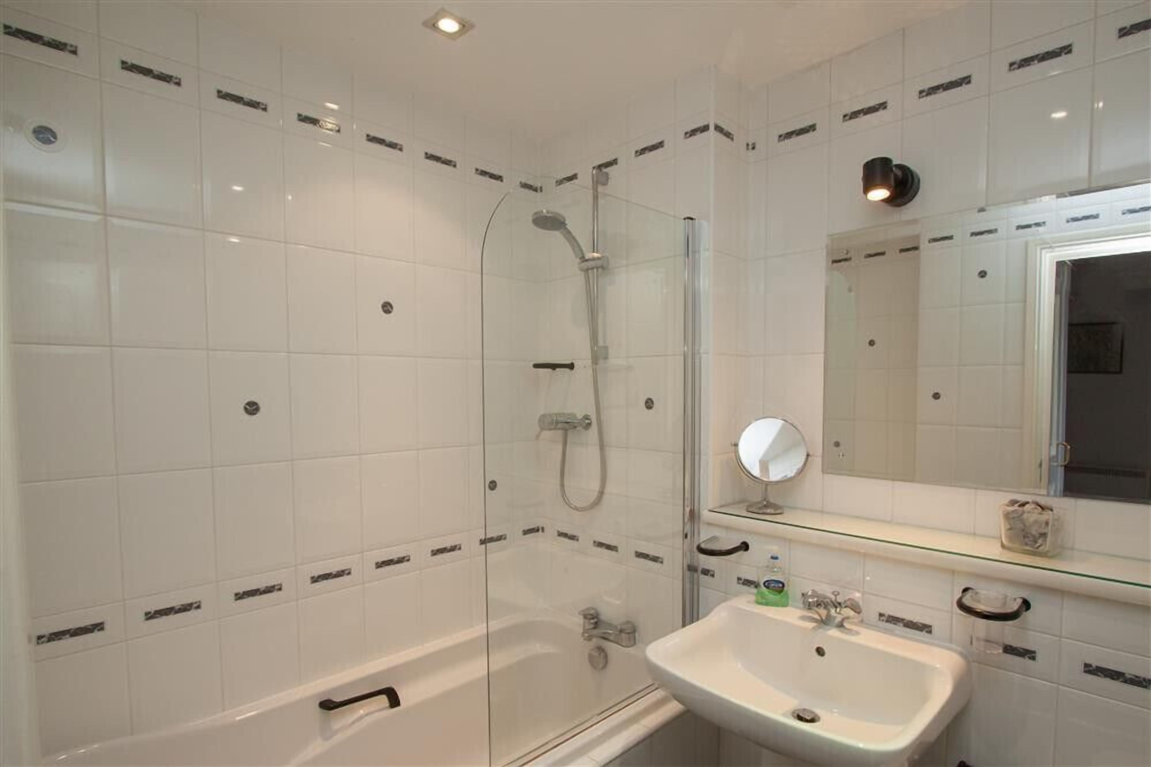 A bathroom with a glass-enclosed shower, a white bathtub, and a sink with a mirror above it.