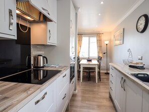 A modern kitchen with white cabinetry, a black induction cooktop, and a dining area with a table and chairs. - Fairview (Windermere)