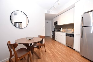 A modern kitchen with white cabinets, stainless steel appliances, and a wooden dining table with chairs.