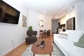 A modern living room with a sofa, a coffee table, a TV mounted on the wall, and a dining area with chairs and a table.