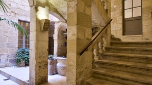 A stone staircase with a wooden handrail leading to an upper level. There are stone arches and columns, and a patterned floor. - Rose Of Rhodes Palazzo  (Valletta)