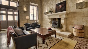 A spacious living room with a fireplace, leather sofas, a coffee table, and a stone wall. - Rose Of Rhodes Palazzo  (Valletta)