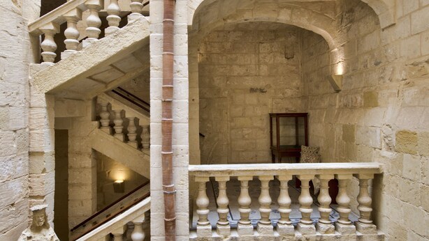 A multi-level stone interior with a central staircase, balconies, and a statue. - Rose Of Rhodes Palazzo  (Valletta)