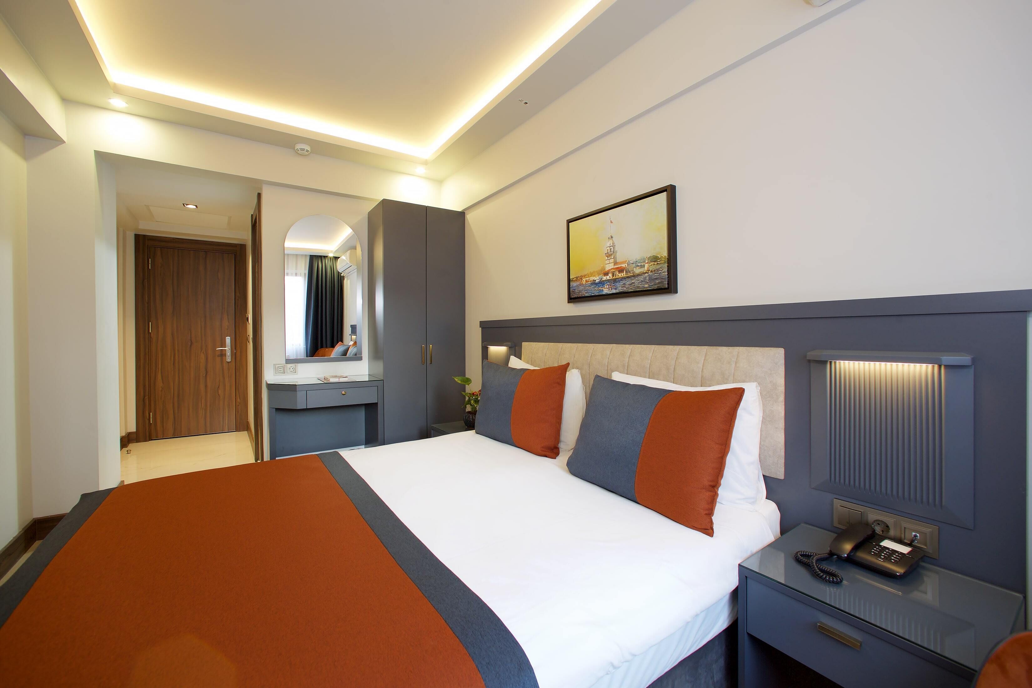 Quarto de hotel com uma cama grande, uma mesinha de cabeceira com telefone e um quadro na parede.